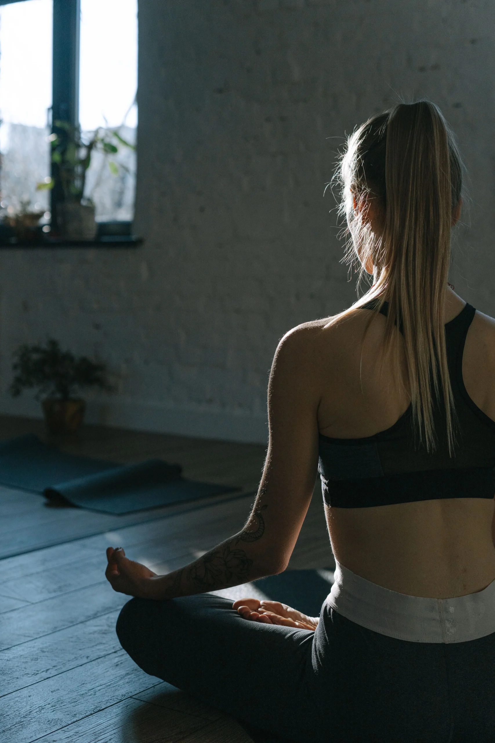 mulher meditando de costas em ambiente interno, postura sentada para iniciantes