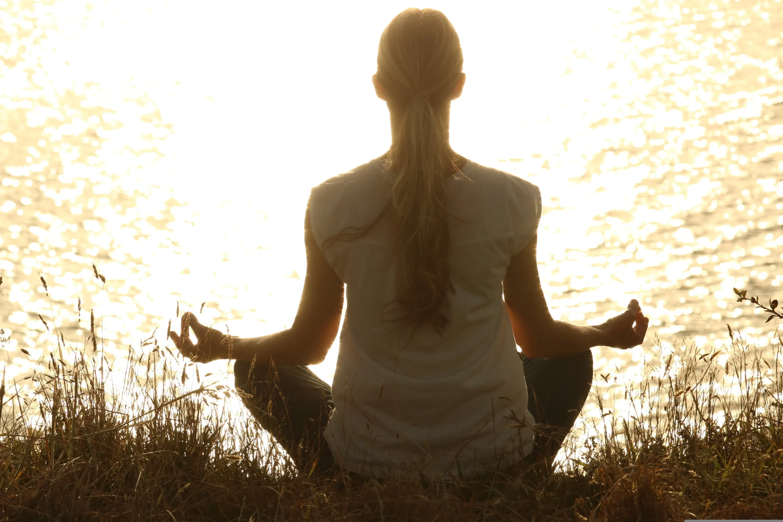 meditação para iniciantes: mulher meditando de costas à beira da água ao pôr do sol